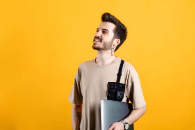 Sarı arka planda izole edilmiş rahat kıyafetler giyen yakışıklı genç adam dizüstü bilgisayarında poz veriyor. Uzaklara bakıyorum..