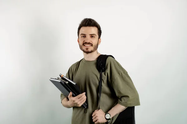 Handsome caucasian man wearing khaki t-shirt posing isolated over white background student with books and backpack and looking at the camera. High school university college concept.
