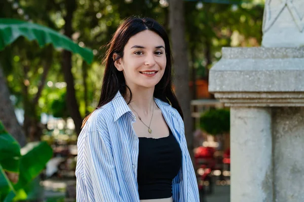 Şehir parkında dikilip poz verirken kameraya bakan esmer kadın portresi. Doğal güzellik konsepti. Güzel kız. Güzel genç bayan..