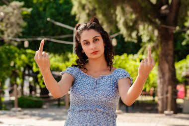 Young brunette woman wearing summer dress on city park, outdoors doing fuck you bad expression, provocation and rude attitude.