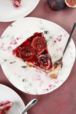 Burgundy yüzeyinde beyaz tabakta bir parça kek: koyu kırmızı jöle ve incir dilimli fırında cheesecake yok