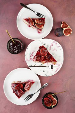 Burgundy yüzeyinde beyaz tabakta bir parça kek: koyu kırmızı jöle ve incir dilimli fırında cheesecake yok