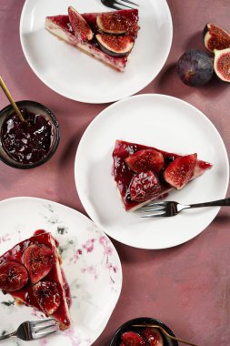 Burgundy yüzeyinde beyaz tabakta bir parça kek: koyu kırmızı jöle ve incir dilimli fırında cheesecake yok