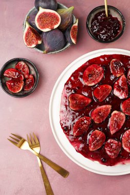 Kırmızı pastanın yarısı kırmızı bir tabakta bordo bir yüzey üzerinde: koyu kırmızı jöle ve incir dilimli fırında cheesecake yok, üst manzara