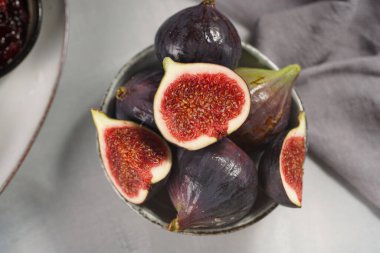 Birkaç sulu kırmızı incir, bir bütün ve gri bir yüzey üzerinde gri bir kasede ikiye bölünmüş.