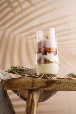 Katmanlı kremalı yoğurtlu uzun bardakta kurabiye, amaretti, kiraz ve kekik tropikal bir ortamda, ahşap bir masa üzerinde keten kumaş üzerinde.