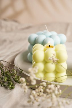 Yeşil, mavi ve beyaz kare baloncuk mumları keten bir masa örtüsünün üzerindeki beton tepside kekik ve çiçek açan dallarla