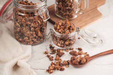 Mısır gevreğiyle fındıklı Mason kavanozu. Tahta kaşık, önüne saçılmış tahıl gevreği ve iki kavanoz tahtadan yapılmış tahtadan küçük tahta tahta.