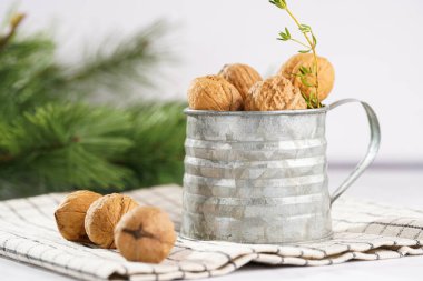 Kareli keten kumaş üzerinde kahverengi ceviz ve beyaz bir masa yüzeyinde Noel ağacı dalı olan metal bir kupa.