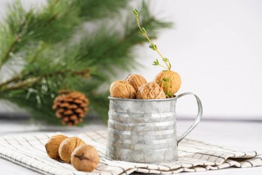 Kareli keten kumaş üzerinde kahverengi ceviz ve beyaz bir masa yüzeyinde Noel ağacı dalı olan metal bir kupa.