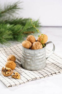 Kareli keten kumaş üzerinde kahverengi ceviz ve beyaz bir masa yüzeyinde Noel ağacı dalı olan metal bir kupa.