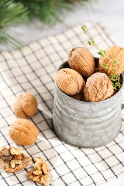 Kareli keten kumaş üzerinde kahverengi ceviz ve beyaz bir masa yüzeyinde Noel ağacı dalı olan metal bir kupa.