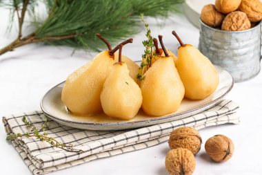 Beyaz oval bir tabakta soyulmuş armutlar damalı keten kumaş ve beyaz bir masa yüzeyinde noel ağacı dalı.