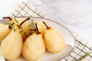 Beyaz oval bir tabakta soyulmuş armutlar damalı keten kumaş ve beyaz bir masa yüzeyinde noel ağacı dalı.