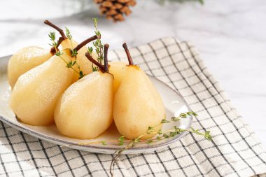 Beyaz oval bir tabakta soyulmuş armutlar damalı keten kumaş ve beyaz bir masa yüzeyinde noel ağacı dalı.