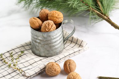 Kareli keten kumaş üzerinde kahverengi ceviz ve beyaz bir masa yüzeyinde Noel ağacı dalı olan metal bir kupa.