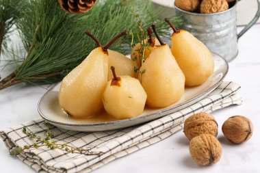 Beyaz oval bir tabakta soyulmuş armutlar damalı keten kumaş ve beyaz bir masa yüzeyinde noel ağacı dalı.