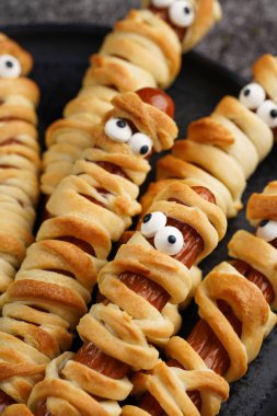 Tatlı Cadılar Bayramı partisi atıştırmalığı: şeker gözlü sosis hamur şeritlerine sarılmış siyah tabakta ketçaplı mumyaları andıran domates sosisi.