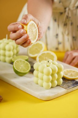 Limon ve kireç dilimleriyle çevrili parlak yeşil bir baloncuk mumuna limon suyu basan kadın elleri, taze kekik.
