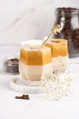 İki bardak, modaya uygun Kore içeceği dalgona kahveli latte. Krem şantili kahve, şeker, sıcak su ve süt katmanları mermer bir tahtanın üzerinde, beyaz yüzey.