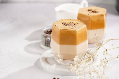 İki bardak, modaya uygun Kore içeceği dalgona kahveli latte. Krem şantili kahve, şeker, sıcak su ve süt katmanları mermer bir tahtanın üzerinde, beyaz yüzey.