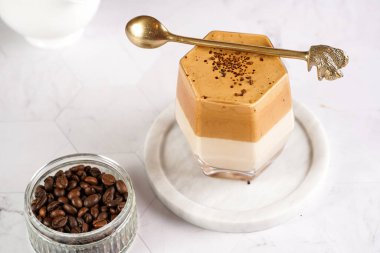 Moda Kore içeceği dalgona kahveli bardak - krem şantili kahve, şeker ve sıcak su ve mermer bir tahtanın üzerindeki süt katmanları, beyaz yüzey