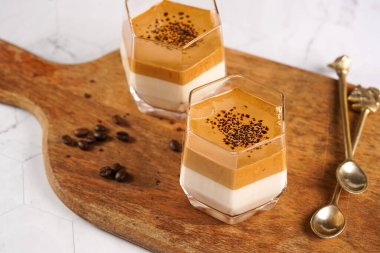 İki bardak modaya uygun Kore içeceği dalgona kahve latte - çırpılmış kahve, şeker ve sıcak su ve beyaz yüzey üzerinde süt katmanları