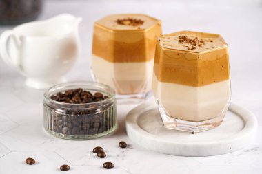 İki bardak modaya uygun Kore içeceği dalgona kahve latte - çırpılmış kahve, şeker ve sıcak su ve beyaz yüzey üzerinde süt katmanları