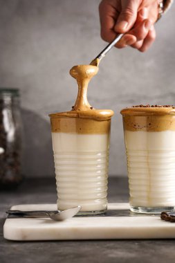 Erkek el karıştırıcı moda Kore içeceği dalgona kahve latte - kremşanti hazır kahve, şeker ve sıcak su ve mermer bir tahtada süt katmanları, gri yüzey