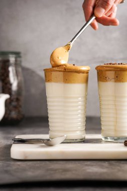 Erkek el karıştırıcı moda Kore içeceği dalgona kahve latte - kremşanti hazır kahve, şeker ve sıcak su ve mermer bir tahtada süt katmanları, gri yüzey