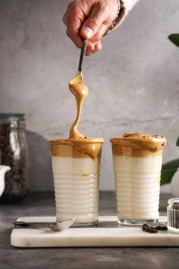 Erkek el karıştırıcı moda Kore içeceği dalgona kahve latte - kremşanti hazır kahve, şeker ve sıcak su ve mermer bir tahtada süt katmanları, gri yüzey