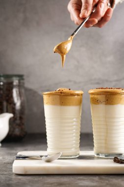 Erkek el karıştırıcı moda Kore içeceği dalgona kahve latte - kremşanti hazır kahve, şeker ve sıcak su ve mermer bir tahtada süt katmanları, gri yüzey