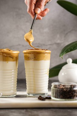 Erkek el karıştırıcı moda Kore içeceği dalgona kahve latte - kremşanti hazır kahve, şeker ve sıcak su ve mermer bir tahtada süt katmanları, gri yüzey