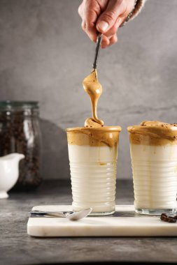 Erkek el karıştırıcı moda Kore içeceği dalgona kahve latte - kremşanti hazır kahve, şeker ve sıcak su ve mermer bir tahtada süt katmanları, gri yüzey