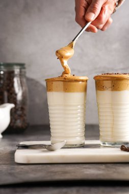 Erkek el karıştırıcı moda Kore içeceği dalgona kahve latte - kremşanti hazır kahve, şeker ve sıcak su ve mermer bir tahtada süt katmanları, gri yüzey