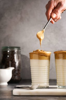 Erkek el karıştırıcı moda Kore içeceği dalgona kahve latte - kremşanti hazır kahve, şeker ve sıcak su ve mermer bir tahtada süt katmanları, gri yüzey