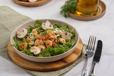 Karides ve şampiyon Arugula salatası, beyaz bir yüzeyde ahşap bir tahtada zeytin yağı ve dereotu.