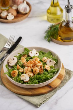 Karides ve şampiyon Arugula salatası, beyaz bir yüzeyde ahşap bir tahtada zeytin yağı ve dereotu.