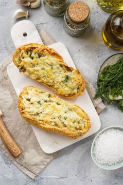 İki parça sarımsaklı ve tereyağlı ekmek - mermer bir tahtanın üzerinde baget, deniz tuzu, biber, dereotu ve sarımsaklı karanfil gri beton arka planda, üst manzara