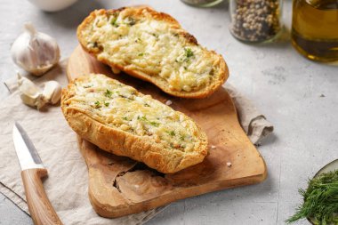 İki parça sarımsaklı ve tereyağlı ekmek - tahtanın üzerinde baget, deniz tuzu, biber, dereotu ve sarımsak karanfili gri beton arka planda, üst manzara