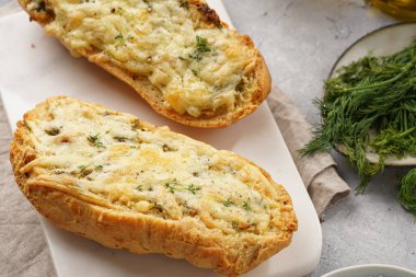 İki parça sarımsaklı ve tereyağlı ekmek - mermer bir tahtanın üzerinde baget, deniz tuzu, biber, dereotu ve sarımsaklı karanfil gri beton arka planda, üst manzara