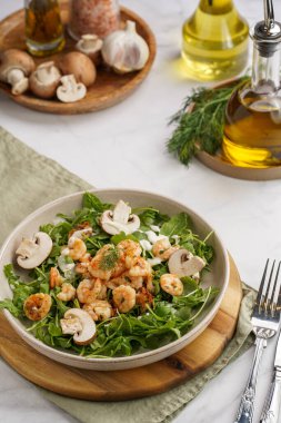 Karides ve şampiyon Arugula salatası, beyaz bir yüzeyde ahşap bir tahtada zeytin yağı ve dereotu.