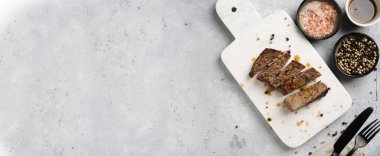 Beyaz mermer tahtada pişmiş biftek dilimlenmiş beyaz ve siyah akranlar, kaba deniz tuzu. Üst görünüm, negatif boşluk, pankart