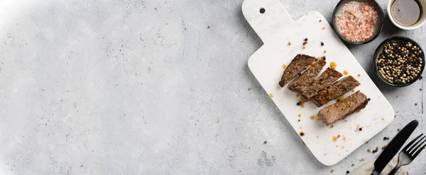 Beyaz mermer tahtada pişmiş biftek dilimlenmiş beyaz ve siyah akranlar, kaba deniz tuzu. Üst görünüm, negatif boşluk, pankart