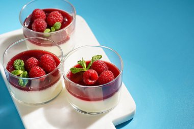 İtalyan sütlü tatlı panna cotta ahududu reçeli ve mermer tahtada taze ahududu, mavi yüzey, negatif alan