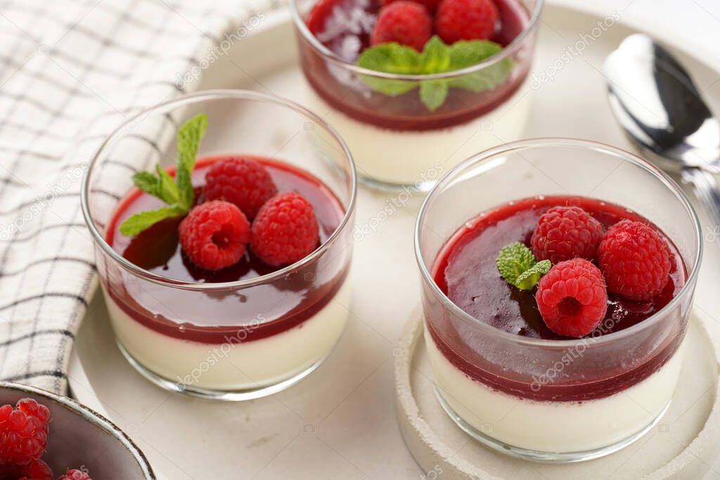 Italian dairy dessert panna cotta with raspberry jam, fresh raspberries and mint on round concrete tray