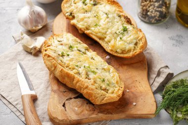 İki parça sarımsaklı ve tereyağlı ekmek - tahtanın üzerinde baget, deniz tuzu, biber, dereotu ve sarımsak karanfili gri beton arka planda, üst manzara