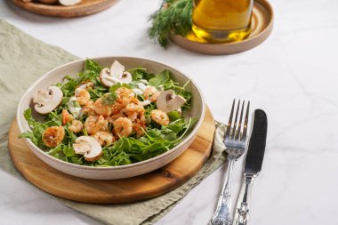 Karides ve şampiyon Arugula salatası, beyaz bir yüzeyde ahşap bir tahtada zeytin yağı ve dereotu.