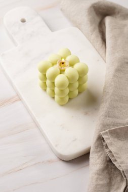 Mermer bir mutfak tahtasının üzerinde soluk yeşil kare baloncuk mumu, bembeyaz keten kumaşla.