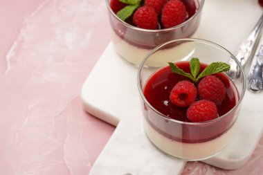 İtalyan sütlü tatlı panna cotta ahududu reçeli, taze ahududu ve pembe yüzeyde mermer tahtada naneli.